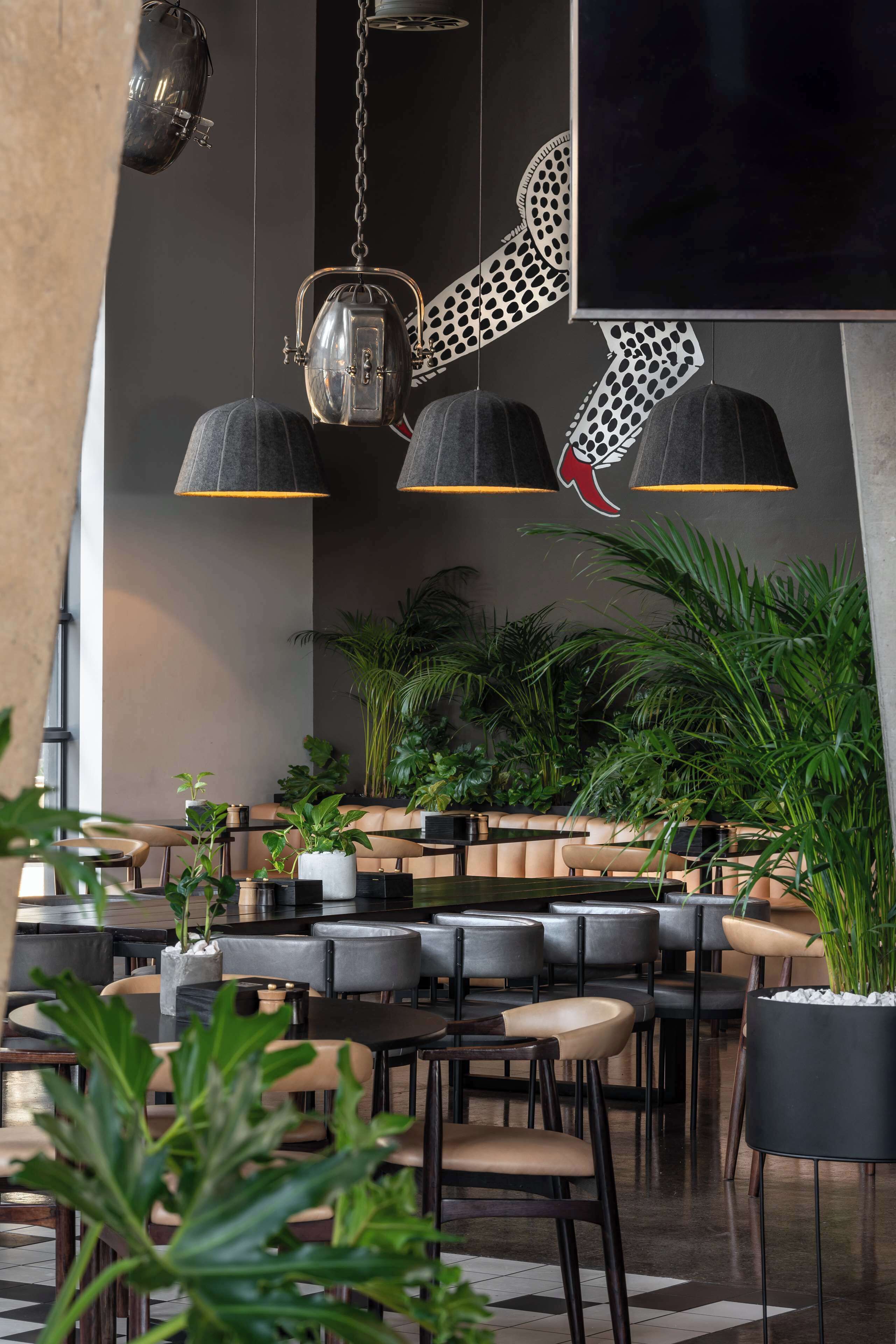 Un restaurante moderno con asientos negros y color beige, lámparas colgantes y plantas en macetas.