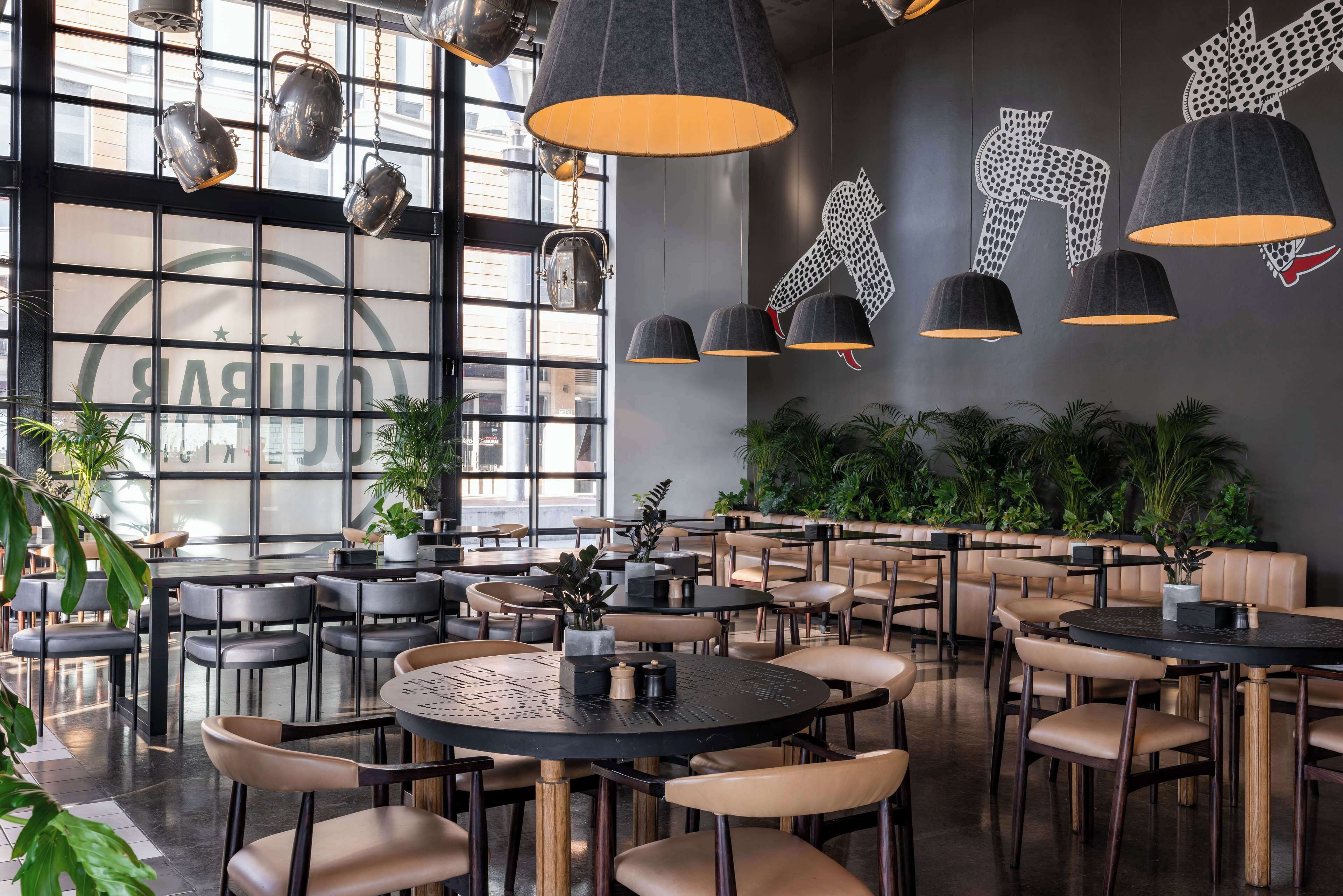 Una cafetería moderna con mesas y sillas redondas, lámparas colgantes y un amplio ventanal con vistas.