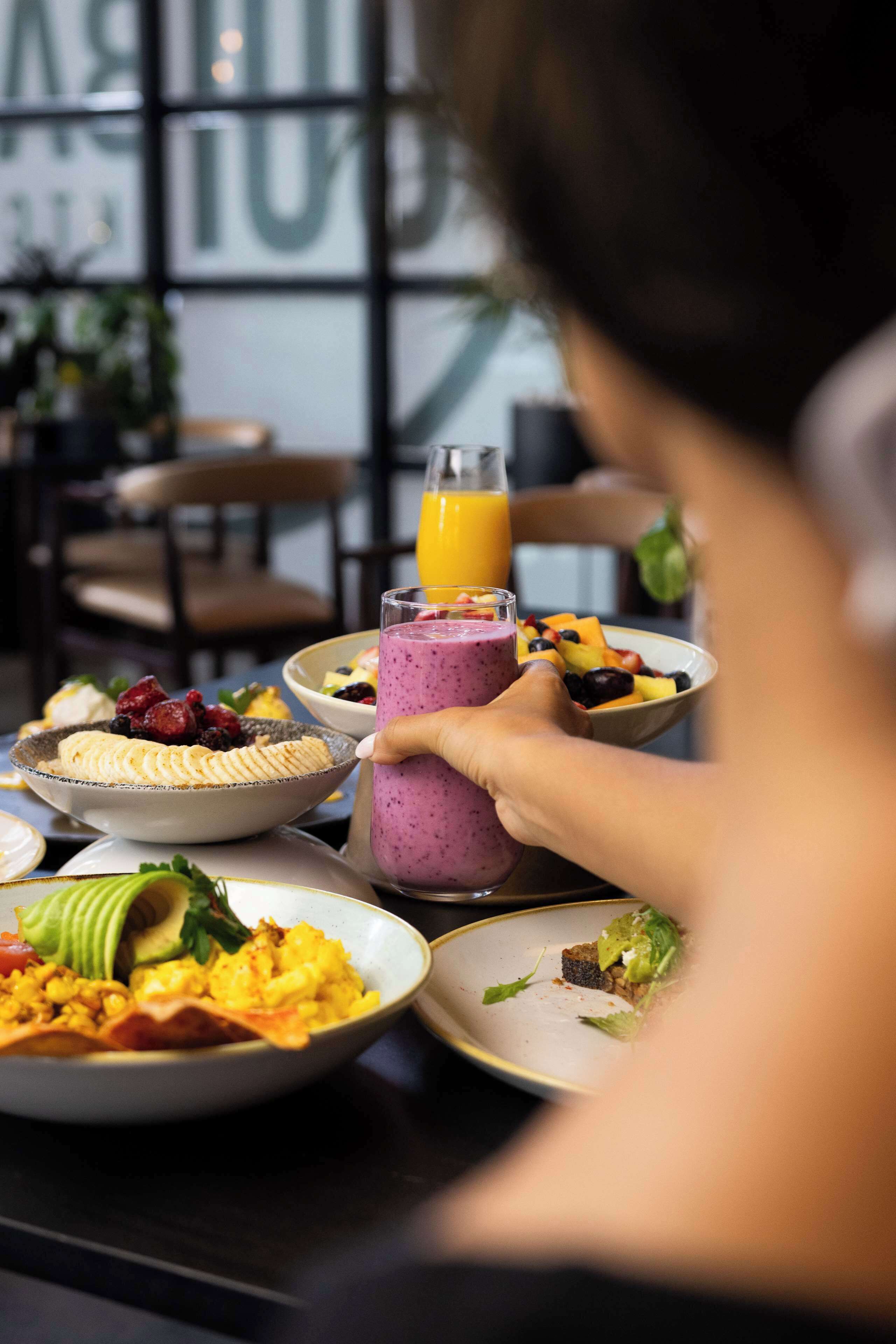 A dining table with various dishes, including a bowl of fruit salad, a plate of scrambled eggs, and a glass of smoothie.
