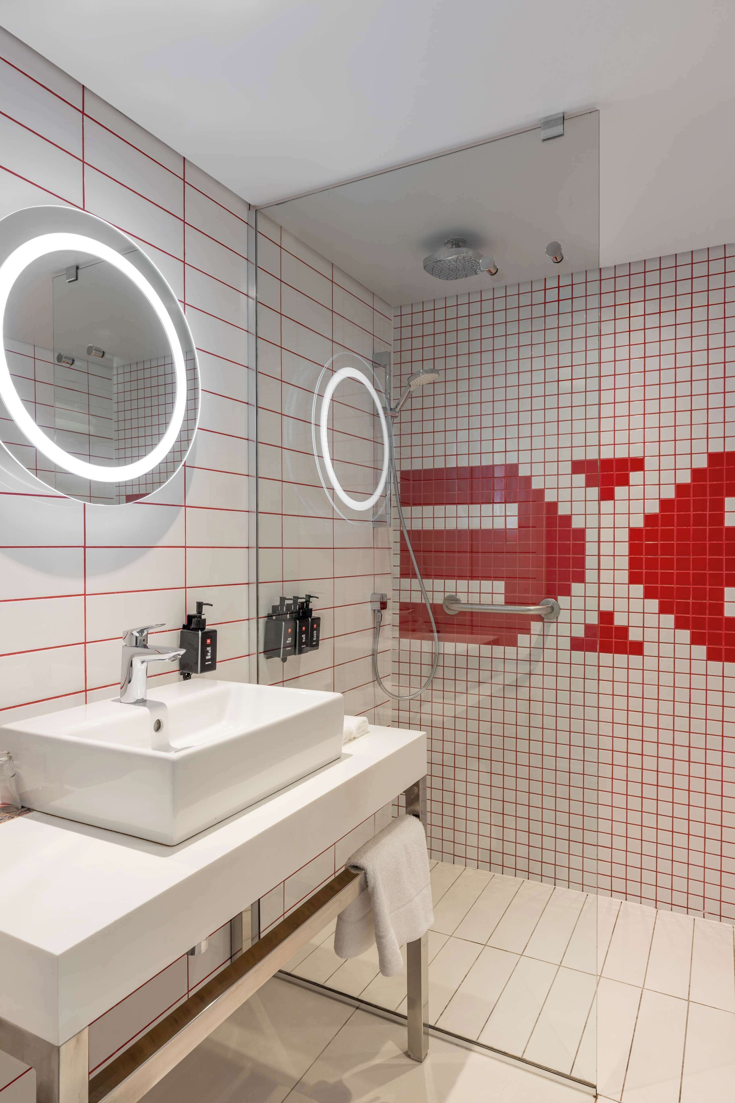 A modern bathroom with a white sink, two mirrors, and a red-tiled wall.