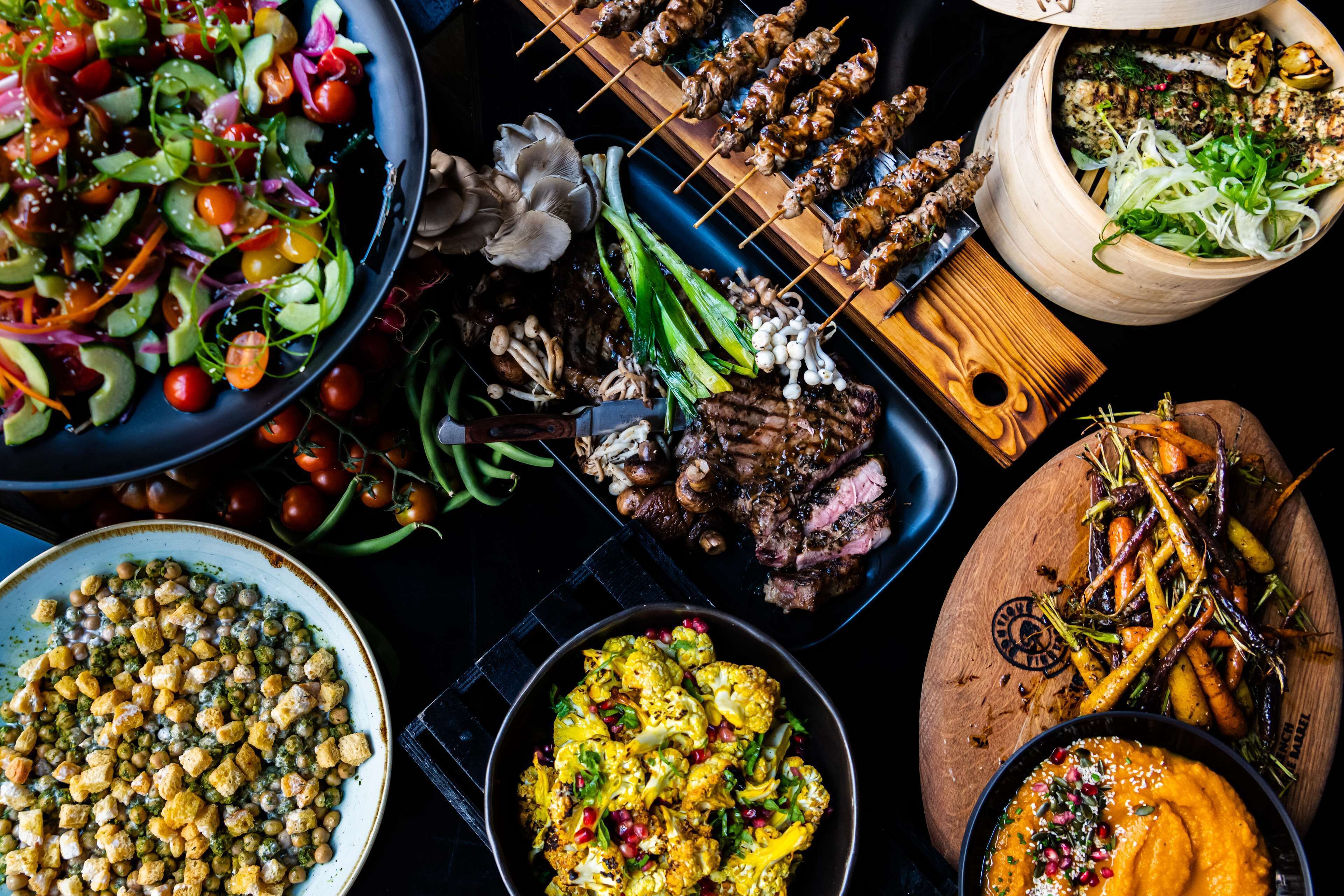 A variety of dishes including skewered meats, grilled vegetables, and a bowl of soup.