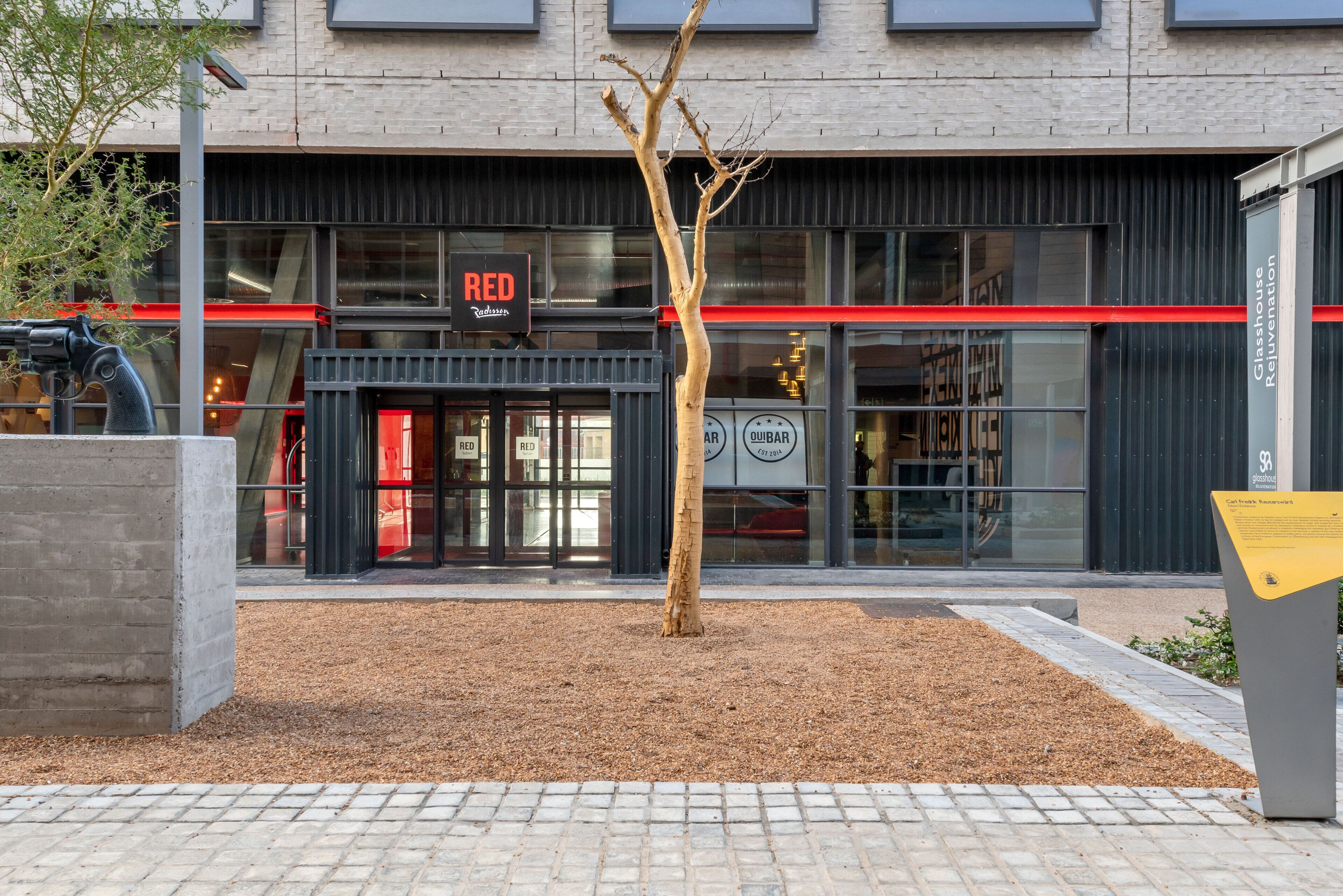 A building with a 'RED' sign above the entrance, a tree in the foreground, and a paved area in front.