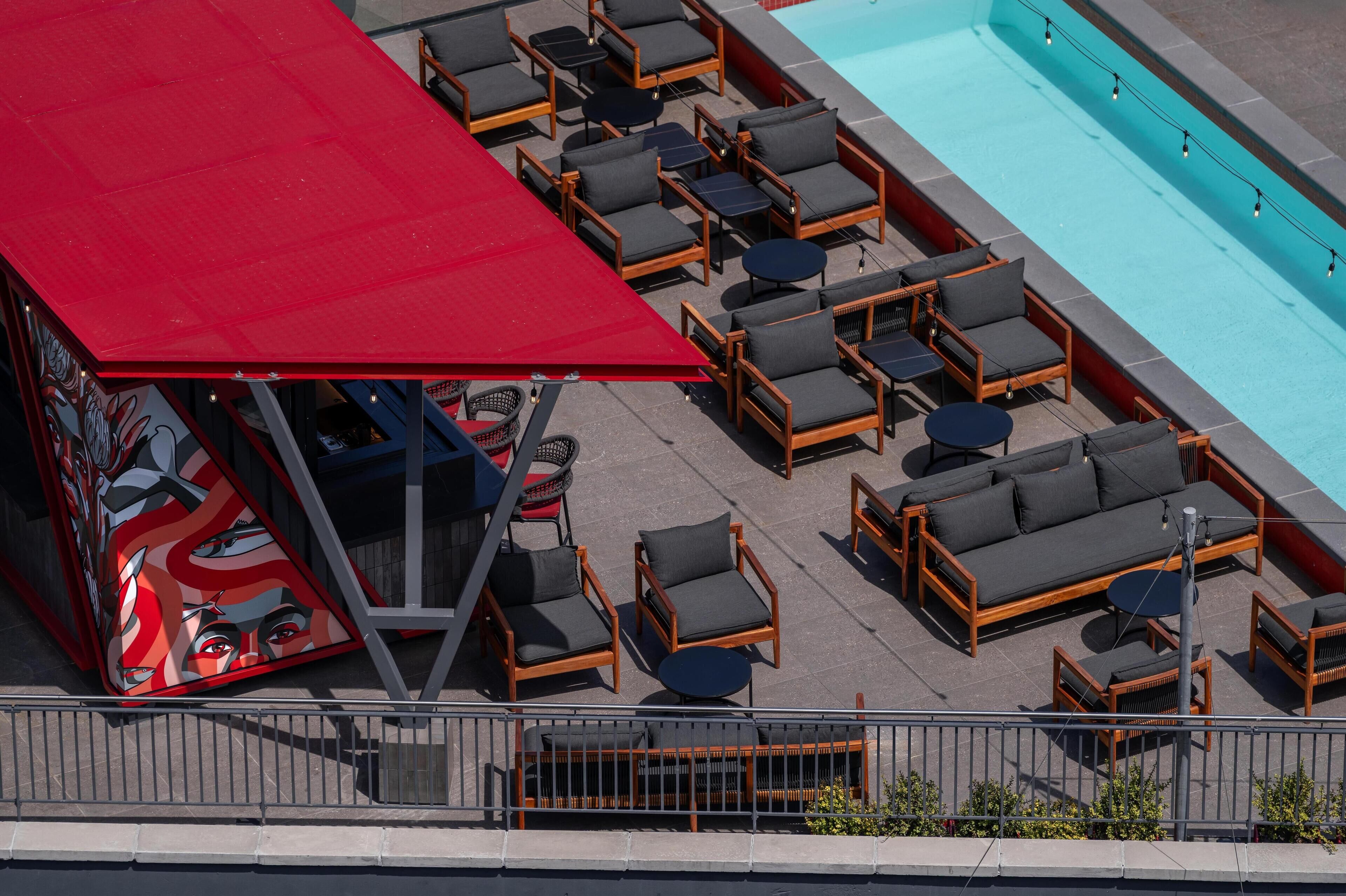 A rooftop pool area with lounge chairs and tables, a red awning, and a mural.