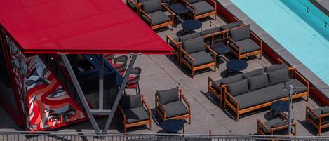 A rooftop pool area with lounge chairs and tables, a red awning, and a mural.