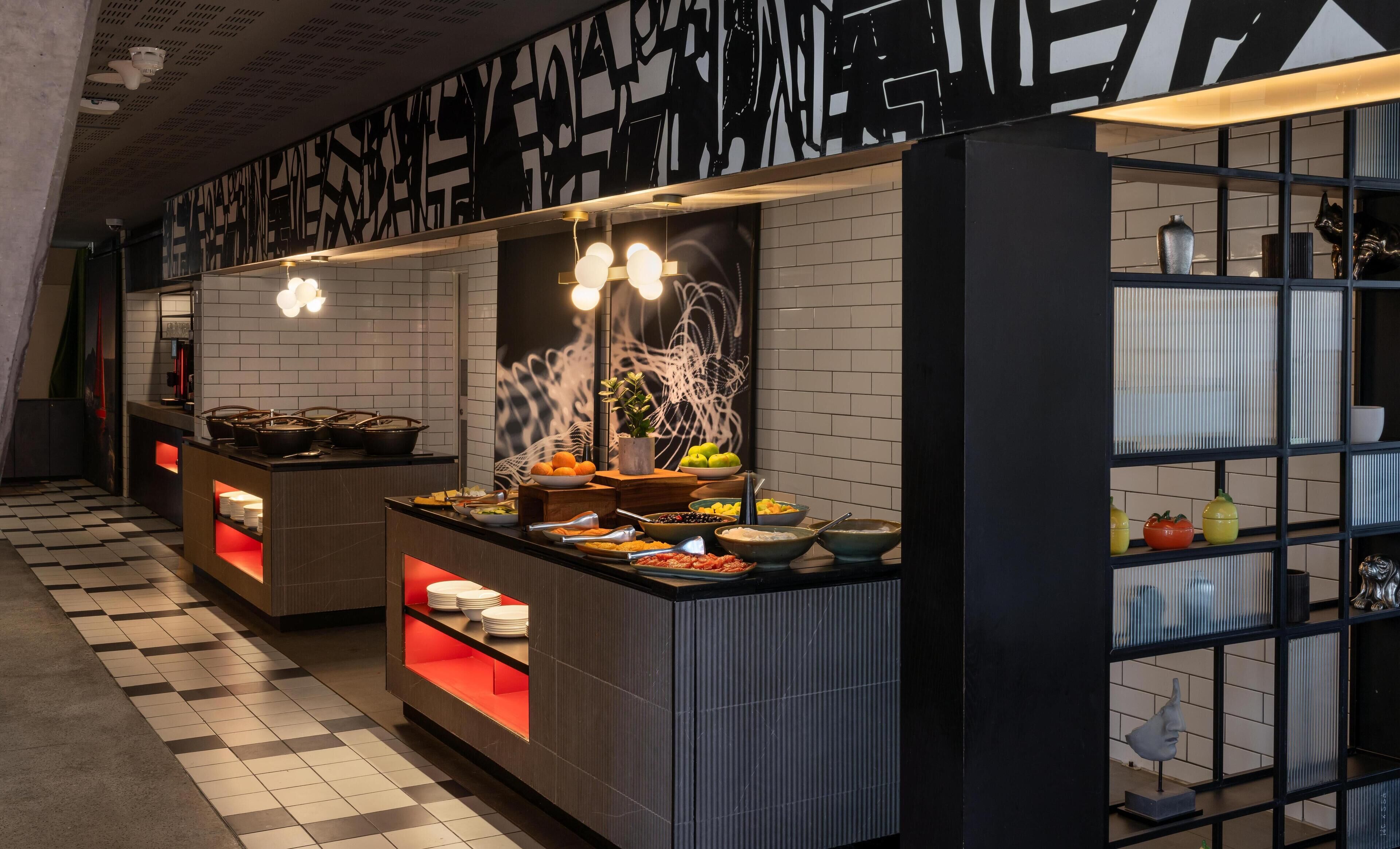 A modern kitchen with checkered flooring, a black and white patterned wall, and a variety of food items displayed on the counter.