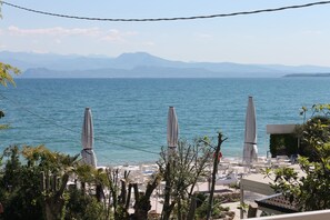 A seaside view with a clear sky, a calm sea, and a row of white umbrellas. - Lake Garda Beach Hostel (Padenghe sul Garda)