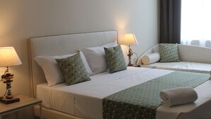 Habitación de hotel con dos camas, cada una con sábanas blancas y almohadas estampadas. Hay lámparas de noche sobre mesitas de madera.