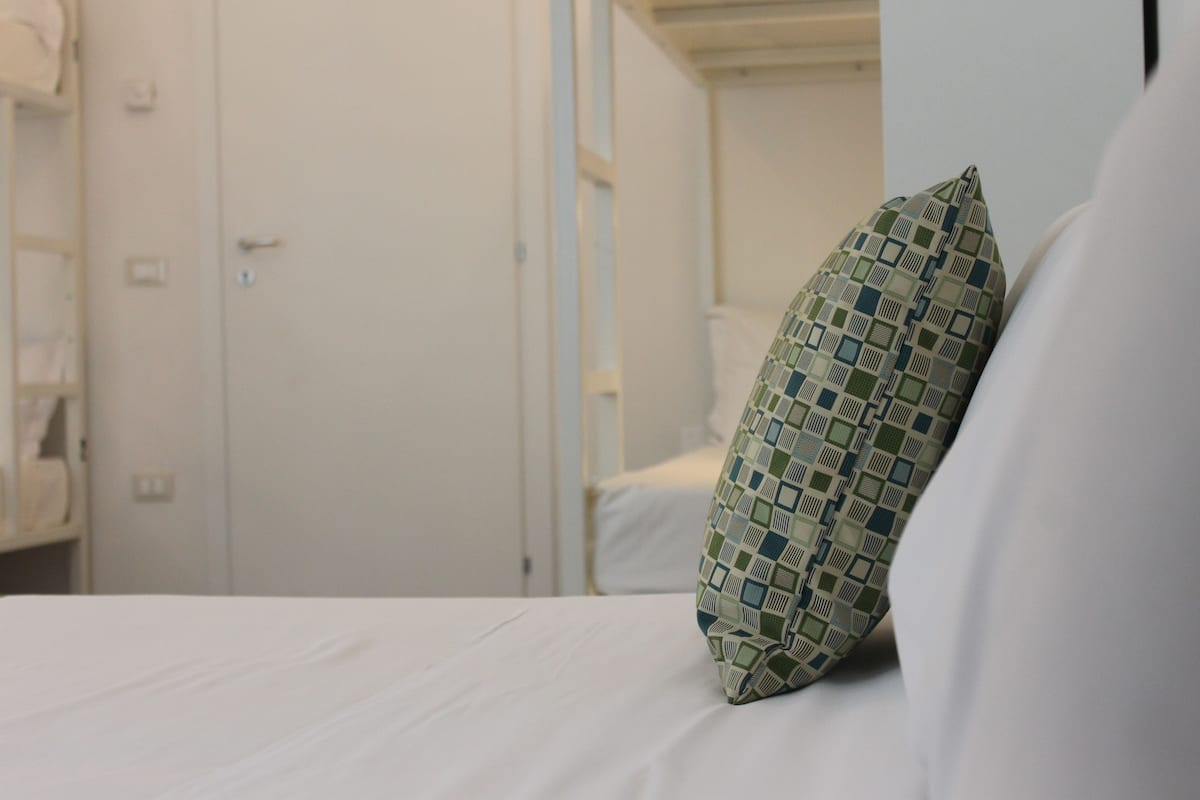 Ein ordentlich bezogenes Bett mit einem gemusterten Kopfkissen und einer weißen Wand im Hintergrund.