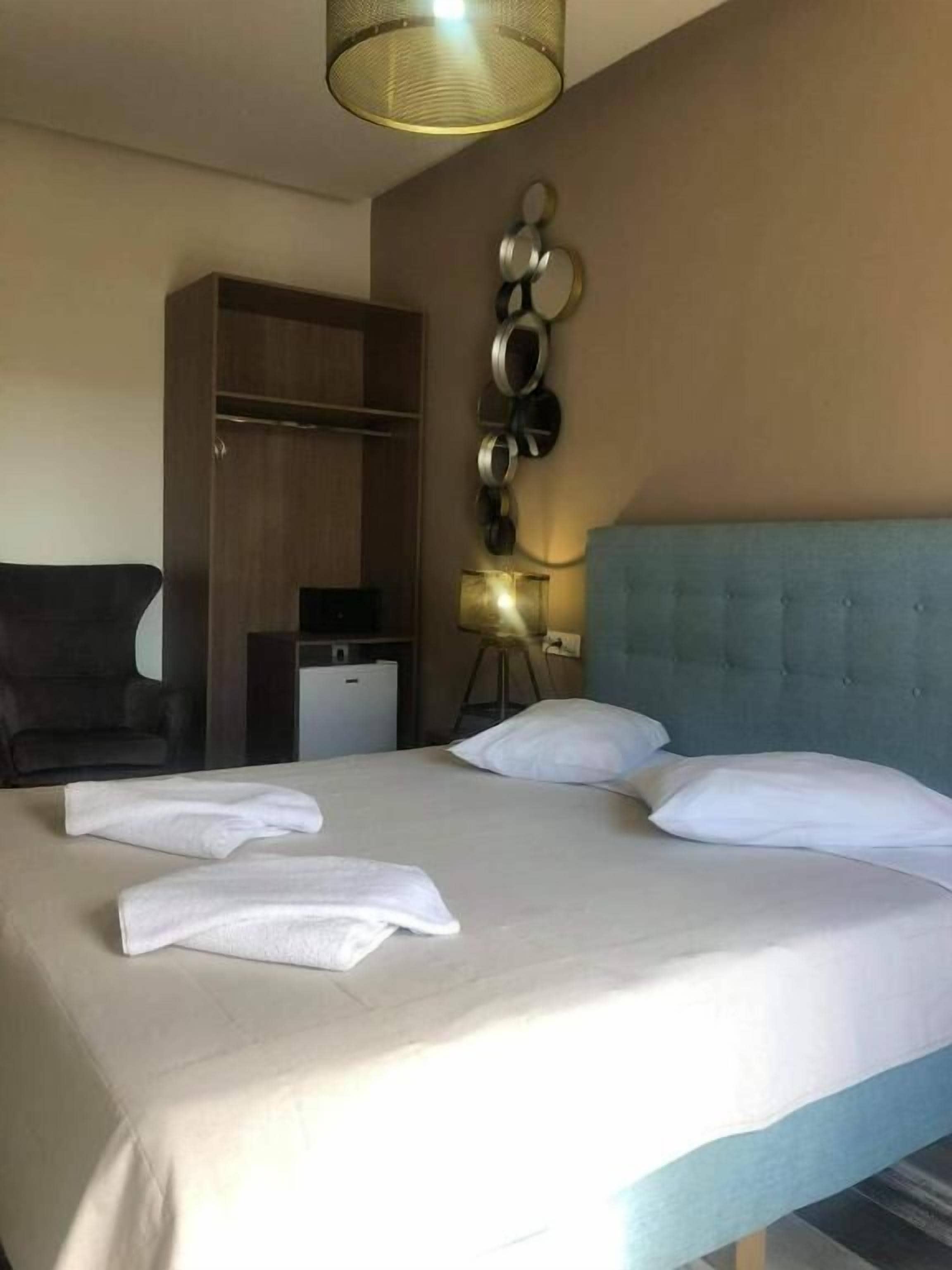 A hotel room with a large bed, a wardrobe, a desk, and a wall-mounted lamp.
