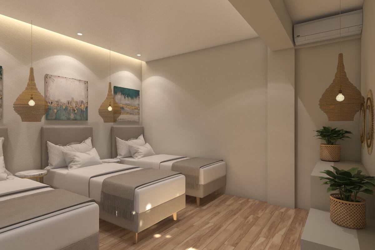 A modern bedroom with two beds, a sofa, and a small table. There are wall-mounted lamps and a potted plant.