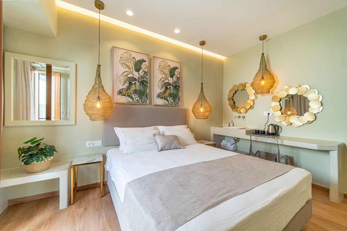 A modern bedroom with a large bed, bedside tables, a bench, a mirror, and two wall-mounted light fixtures.