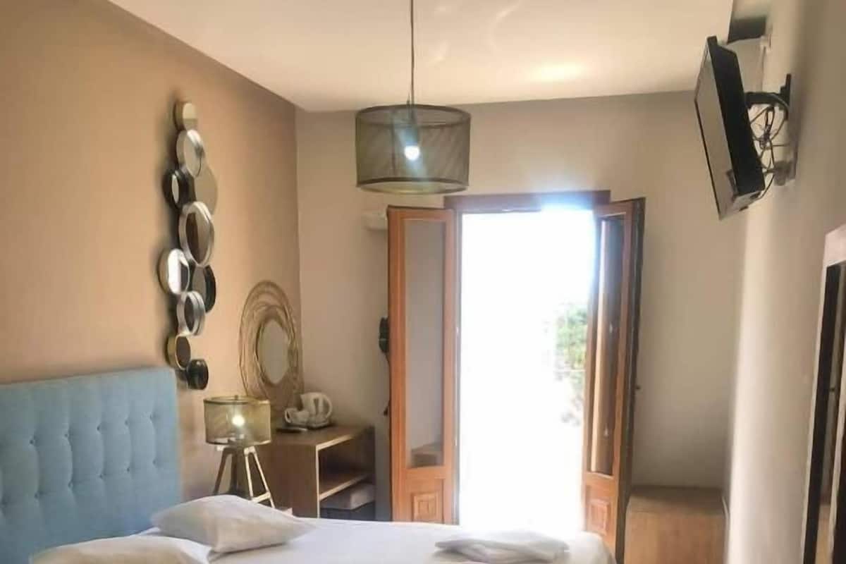 A bedroom with a bed, a chair, a desk, and a mirror.