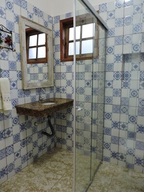 Un baño con cabina de ducha, lavamanos con espejo y azulejos estampados.
