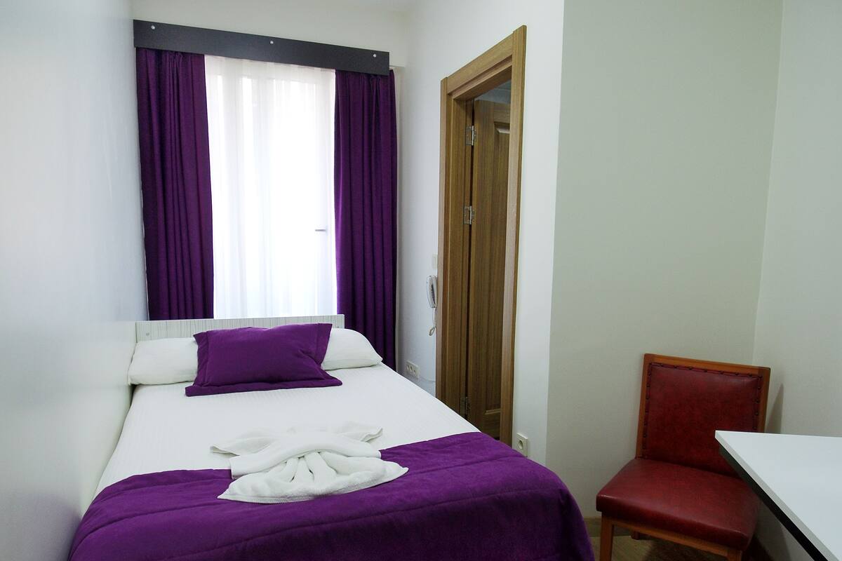A small, neatly arranged bedroom with a bed, a chair, and a desk.