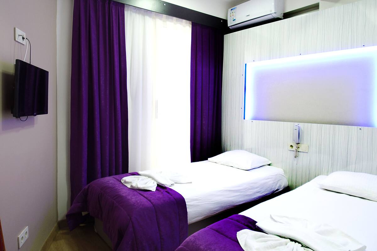A hotel room with two beds, purple bedding, a mounted TV, and an air conditioning unit.