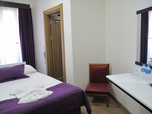 A hotel room with a bed, a chair, a desk, and a mirror.