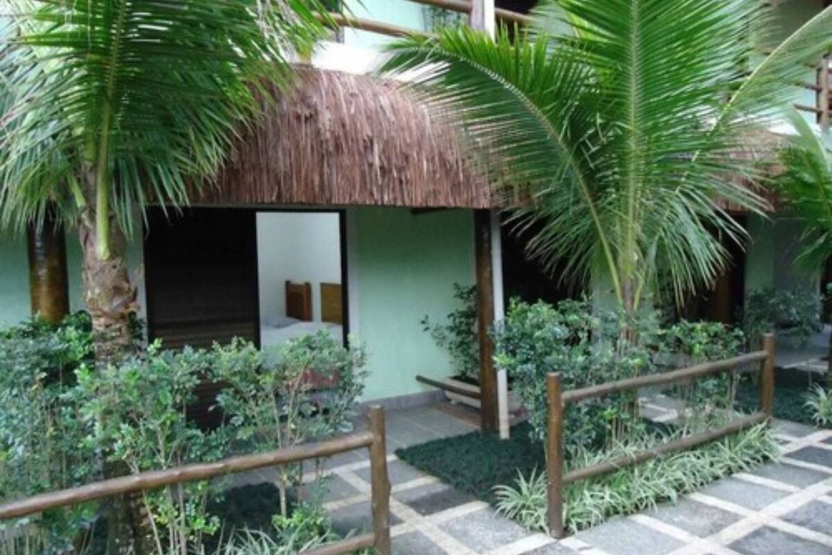 A courtyard with a thatched-roof structure, palm trees, and a tiled floor.