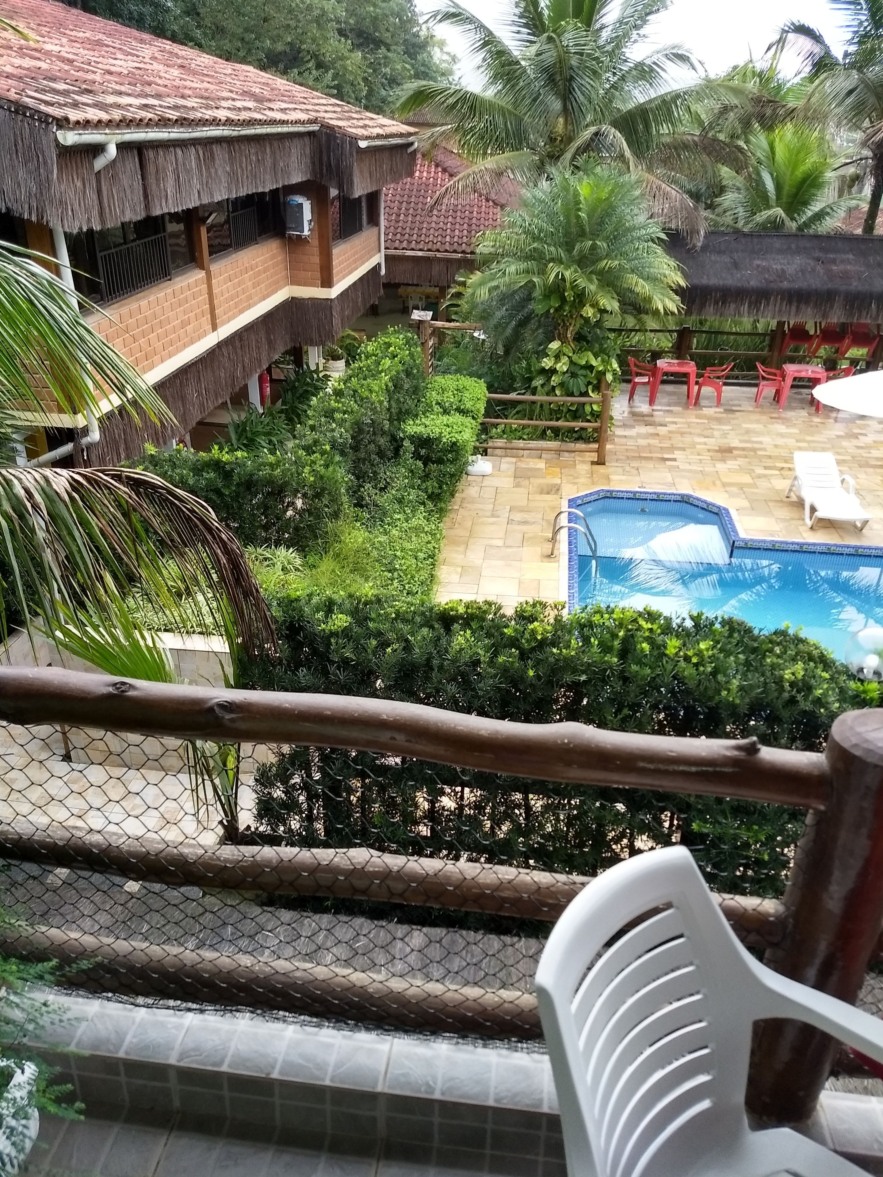 A pool area with a thatched-roof building, palm trees, and a fenced garden.