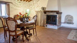 Un comedor con mesa de madera, sillas con motivos florales, chimenea y televisor antiguo.