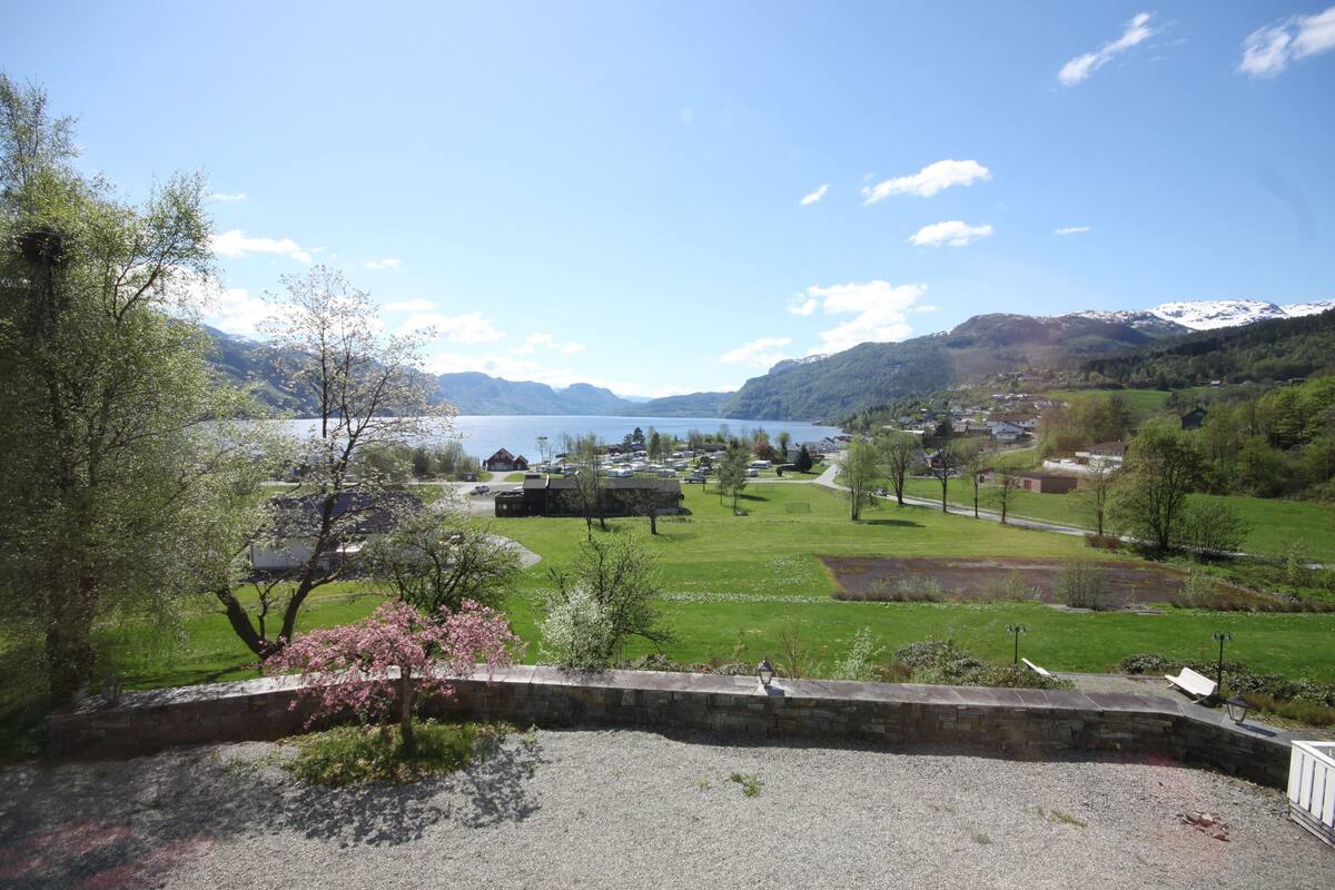 A scenic view of a lake with mountains in the background, a grassy area, and a stone wall in the foreground.