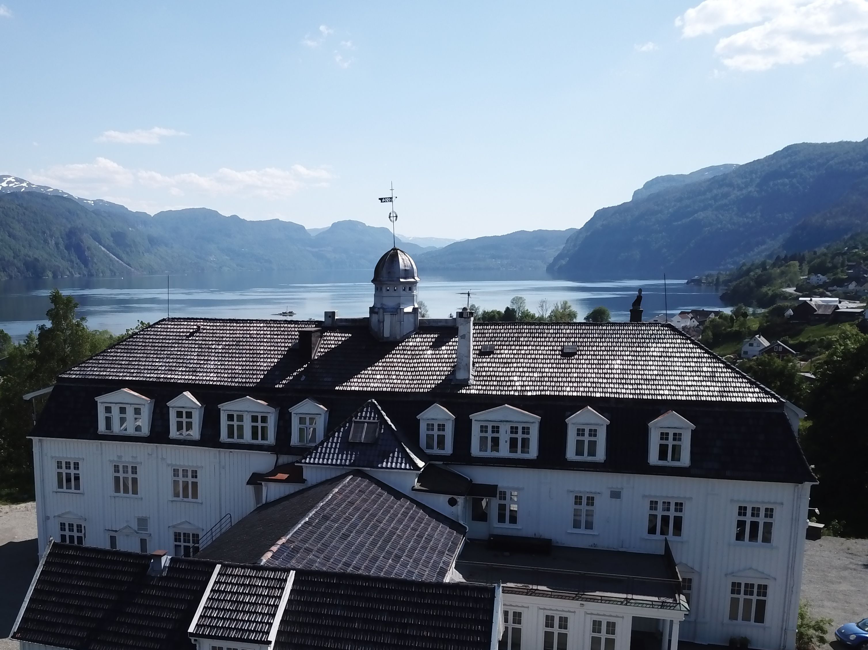 Um edifício grande com uma cúpula imponente e um mastro, rodeado por montanhas e um lago.
