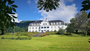 A large, white, multi-story building with a symmetrical facade, surrounded by a well-maintained lawn and trees. - Sauda Fjordhotell (Sauda)