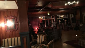 A dimly lit room with wooden paneling, a bar area, and several upholstered chairs.
