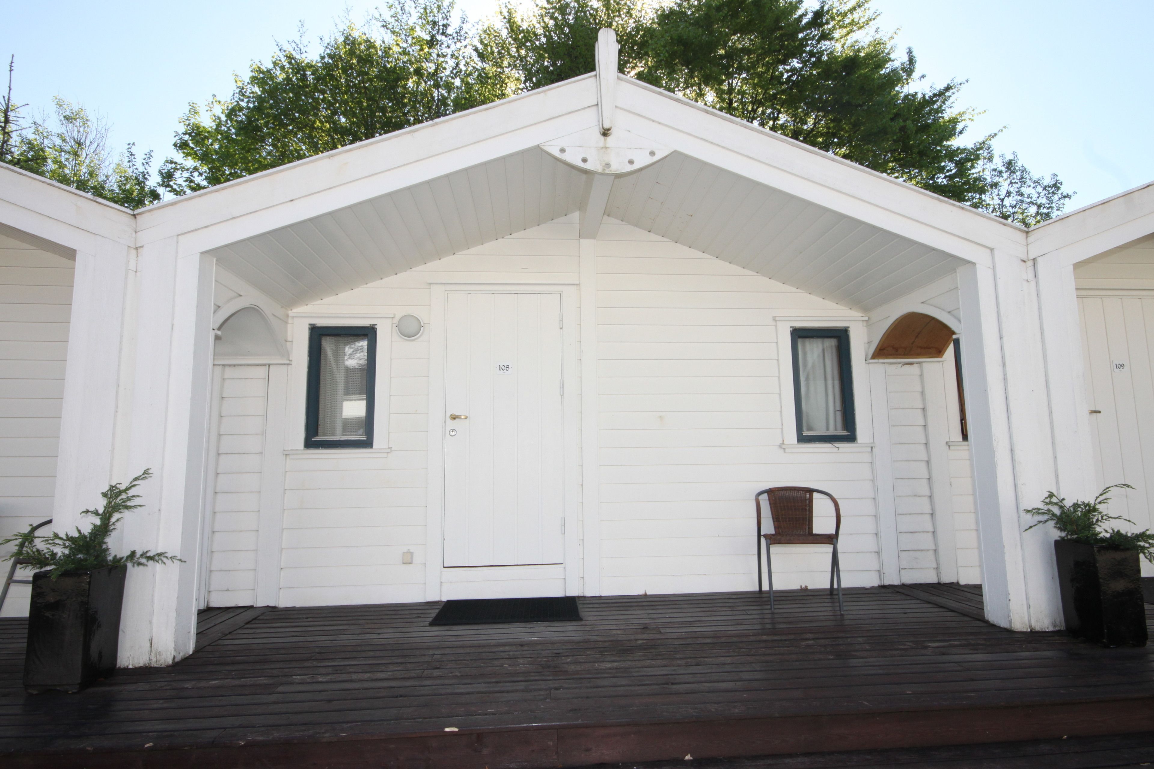 A white building with a porch, two doors, and a chair.