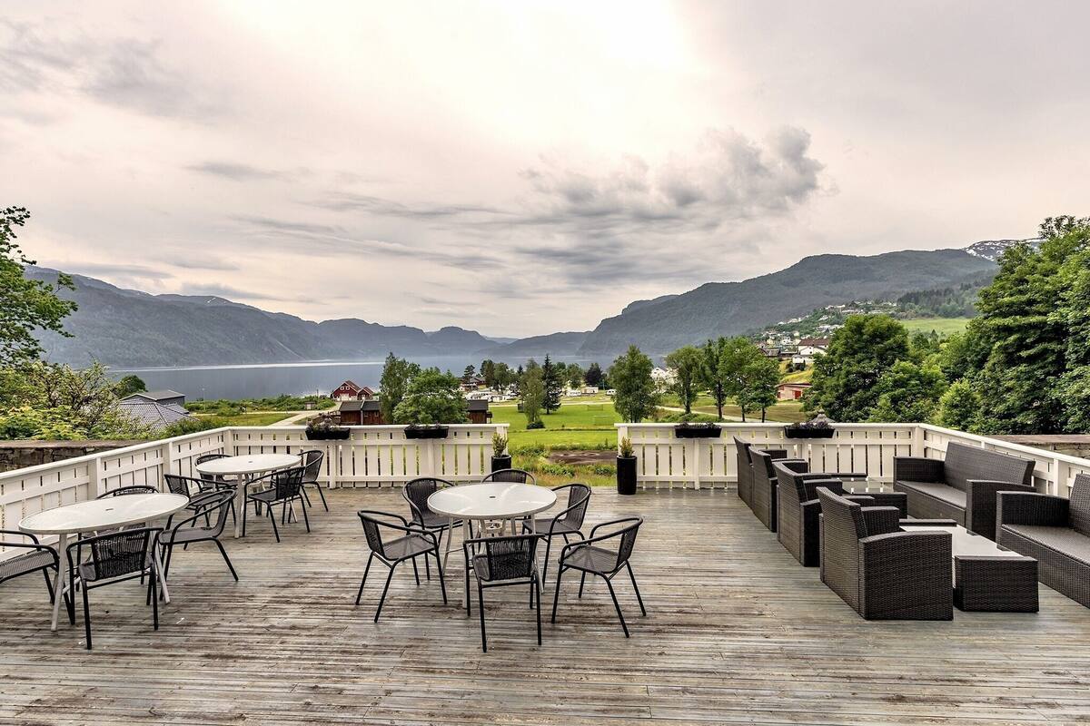 A deck with outdoor seating and a view of a lake and mountains.