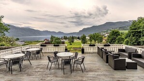 A deck with outdoor seating and a view of mountains and a lake. - Sauda Fjordhotell (Sauda)