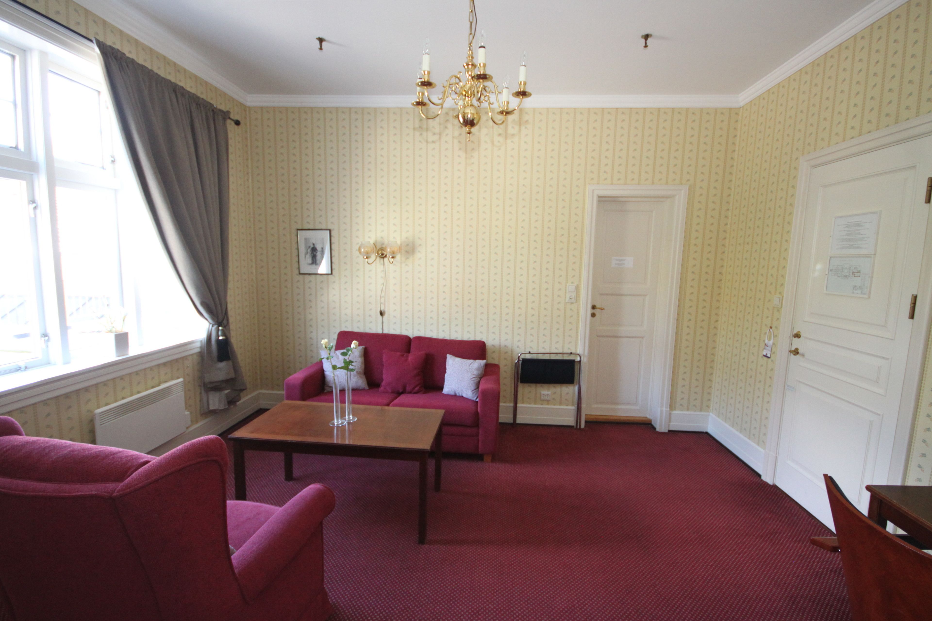 A room with a red carpet, a red sofa, a wooden coffee table, and a chandelier.