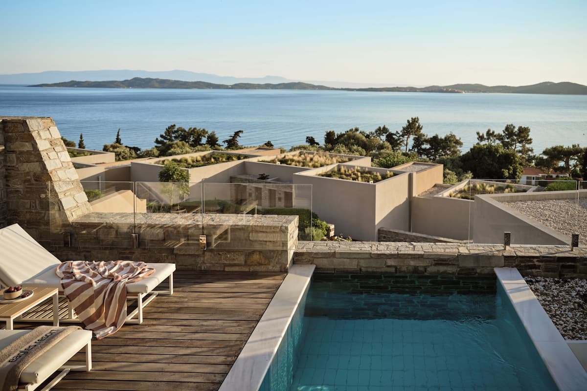 Ein Poolbereich mit Blick auf das Meer, Liegestühle und eine Steinmauer.