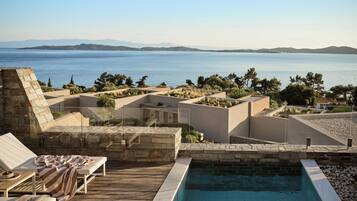 A pool area with a view of the sea, lounge chairs, and a stone wall.