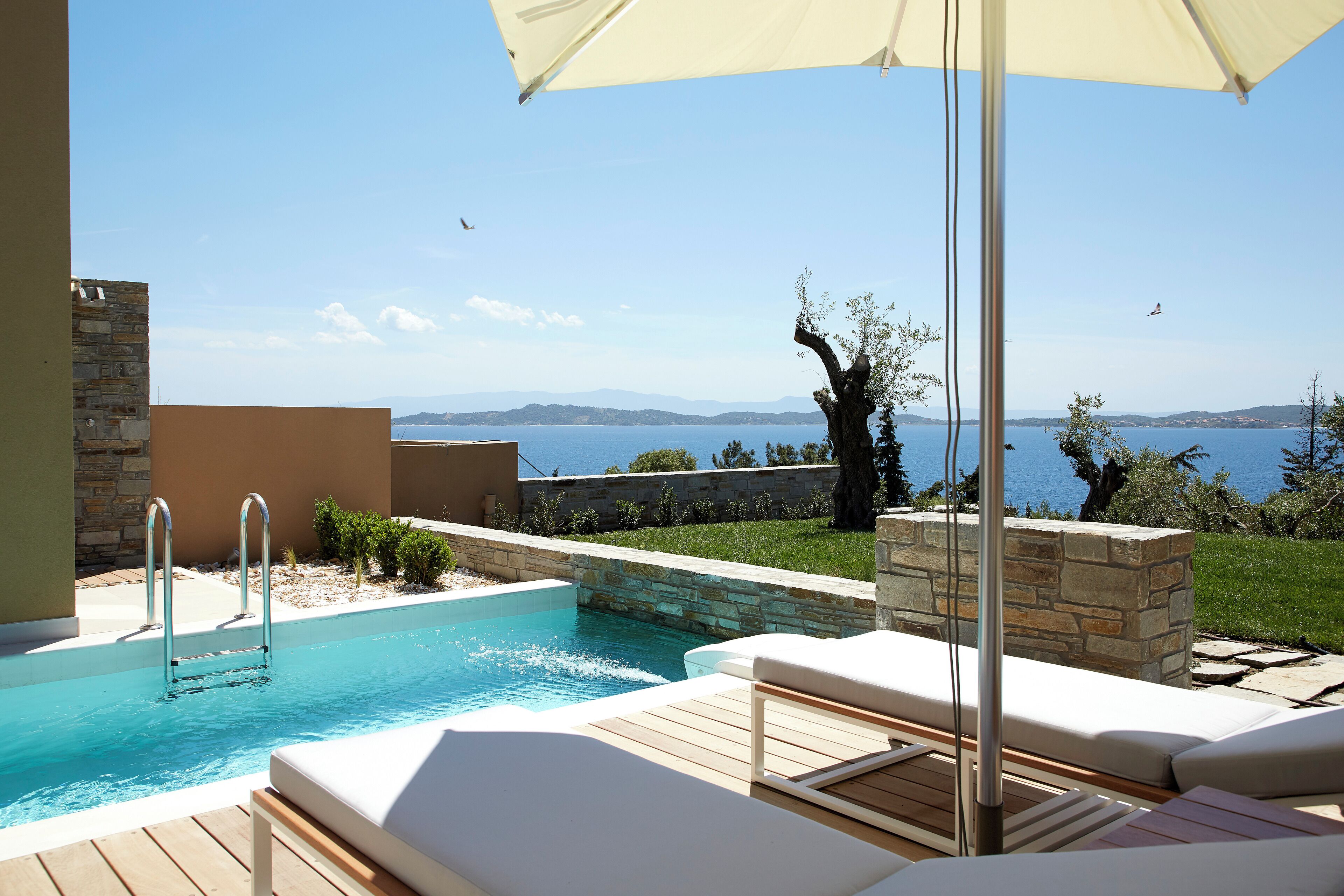 En pool med havudsigt, et loungeområde med et solsejl og en stenvæg.