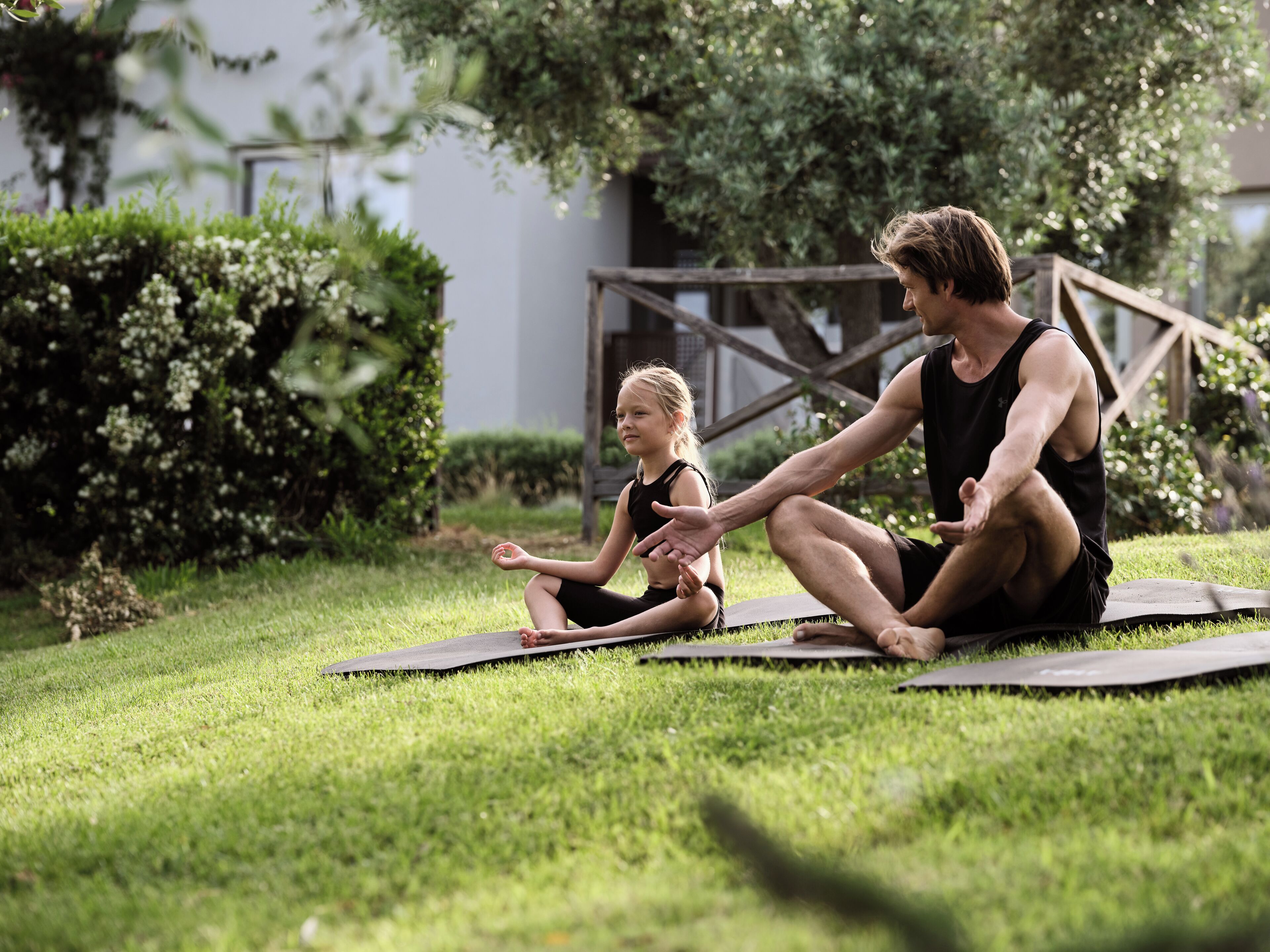 Deux personnes assises sur des tapis de yoga, à l’extérieur, sur l’herbe.