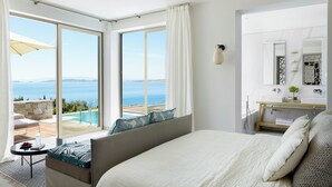 A hotel room with a bed, a small table, a sofa, a bathroom with a mirror, and a view of the sea. - Eagles Villas - Small Luxury Hotels of The World (Aristotelis)