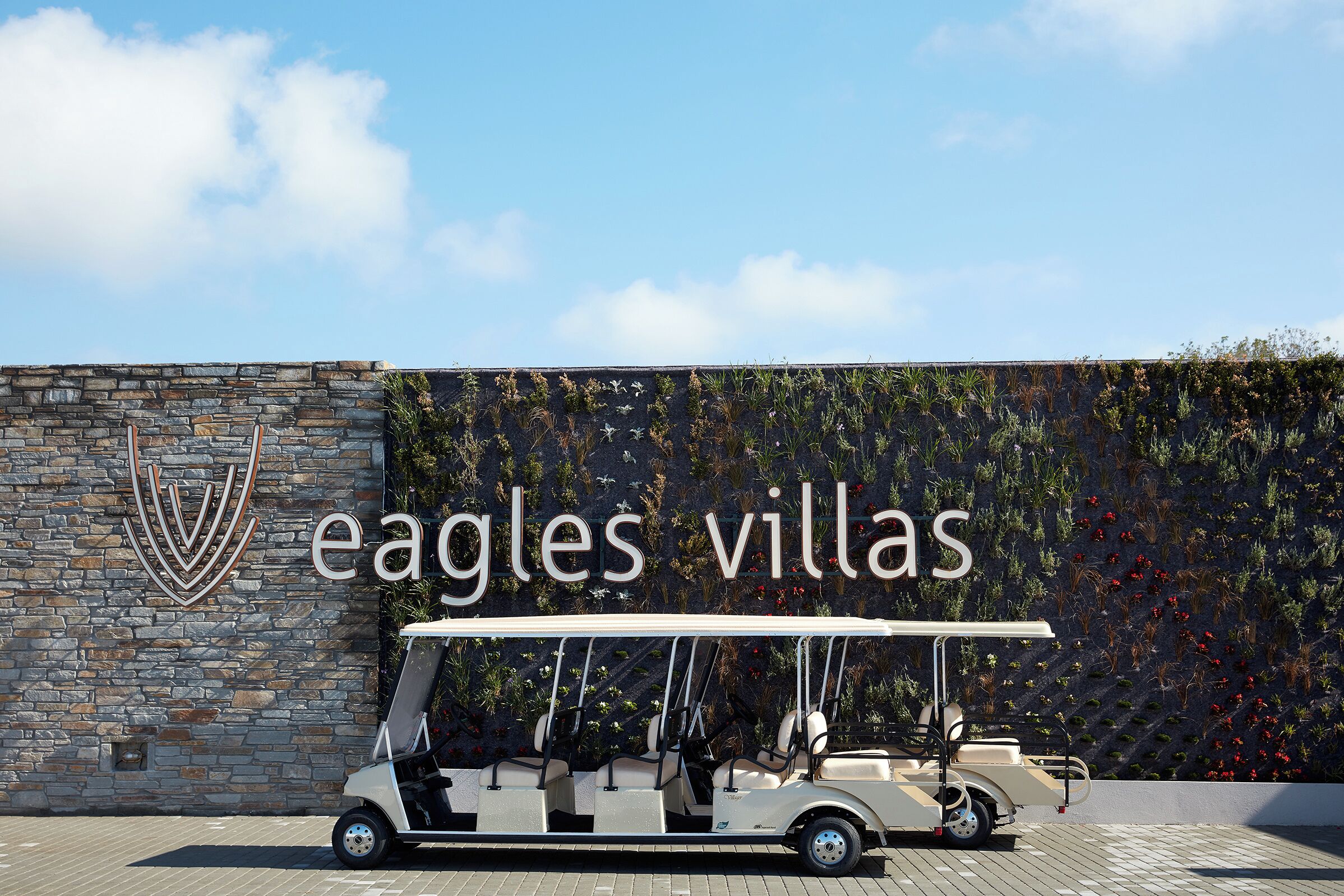 Ein Golfwagen vor einer Mauer mit dem Schriftzug "eagles villas" und einer Steinwand mit einem Logo.