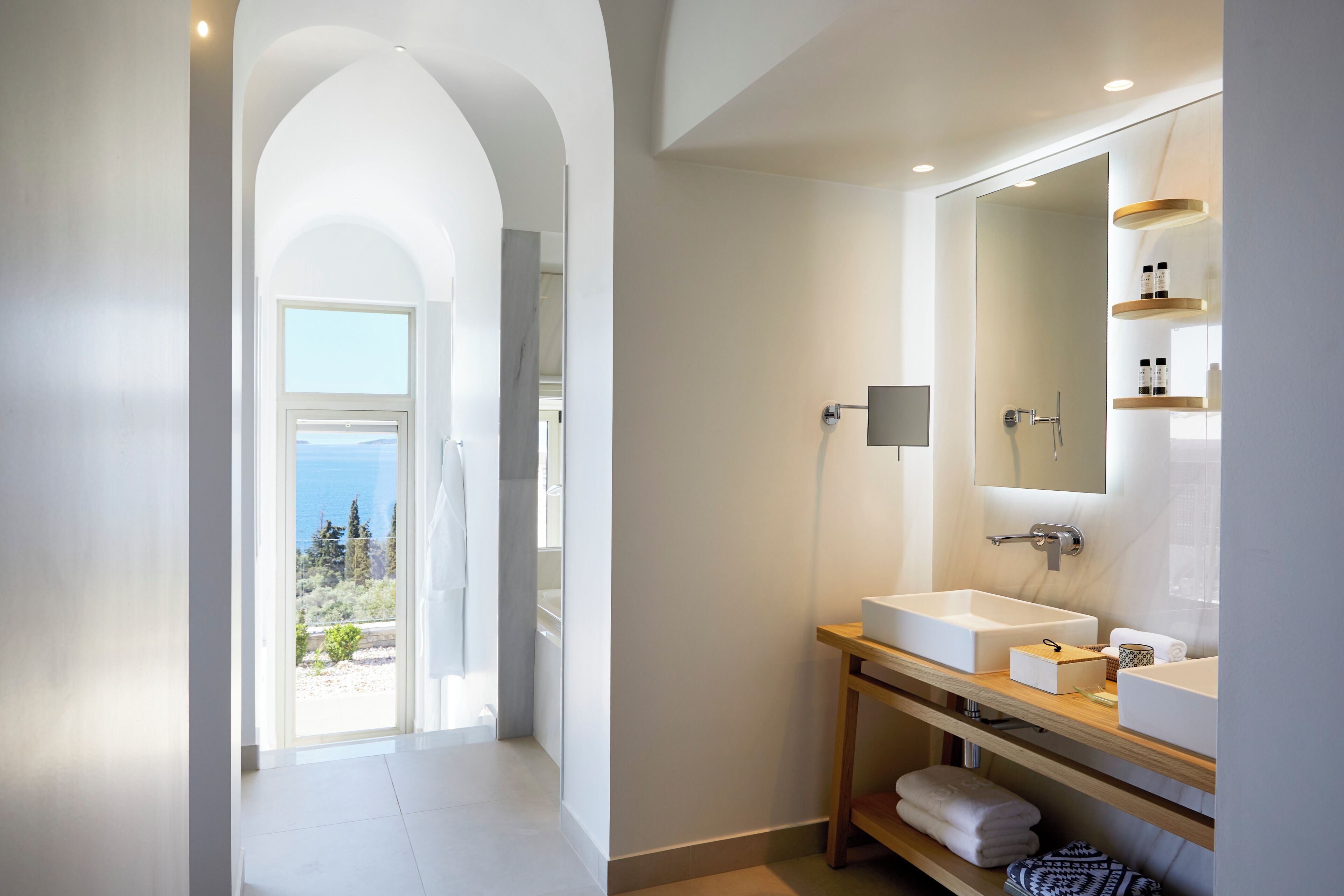A modern bathroom with a large mirror, two sinks, and a view of the sea.