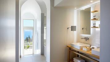 A modern bathroom with a large mirror, two sinks, and a view of the sea.