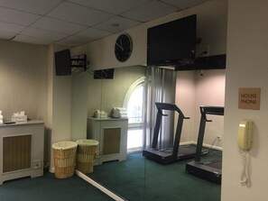 A room with a treadmill, a wall clock, a television, a 'House Phone' sign, and wicker baskets.