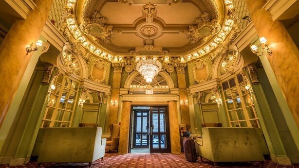 Un hall d’entrée somptueux, orné d’un imposant lustre, de colonnes classiques et d’un sol à motifs.