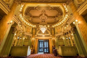 Un hall d’entrée somptueux, orné d’un imposant lustre, de colonnes classiques et d’un sol à motifs.