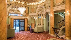 Un hall d’entrée somptueux, orné de colonnes de marbre, d’un lustre et d’un escalier.
