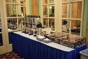 A buffet setup with a coffee machine, stacked plates, and a variety of food items.