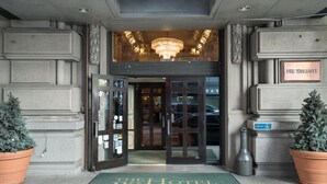 L’entrée de l’hôtel Wolcott, avec un lustre, un paillasson vert et deux plantes en pot.