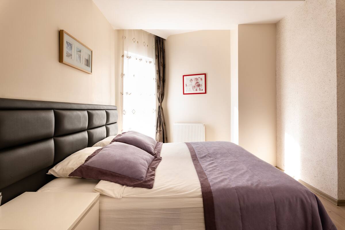 A bedroom with a bed, a nightstand, a radiator, and two framed pictures on the wall.
