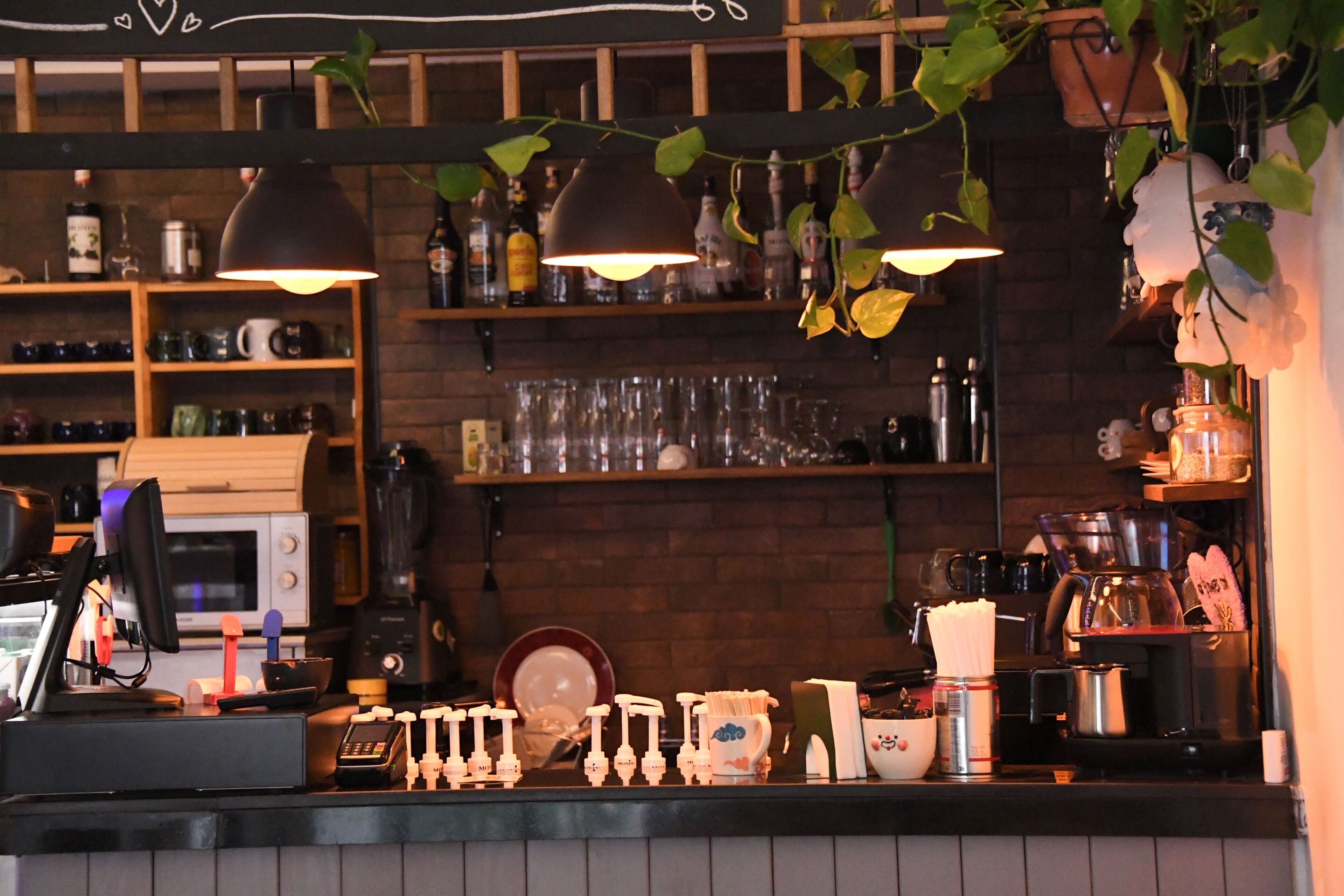 Zona de bar con mostrador, estantes con botellas, vasos y una máquina de café.