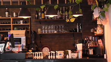 Zona de bar con mostrador, estantes con botellas, vasos y una máquina de café.