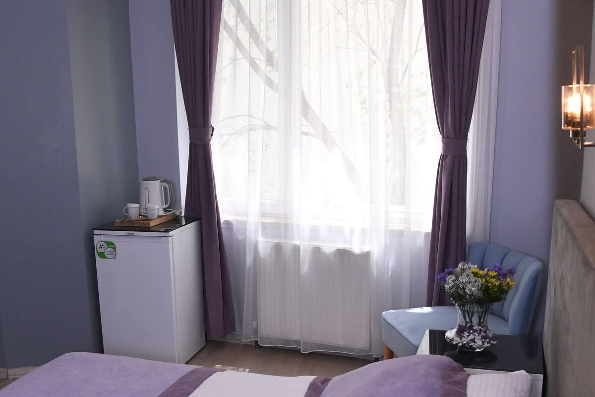 A hotel room with a bed, a small table with a vase of flowers, a coffee maker, and a refrigerator.