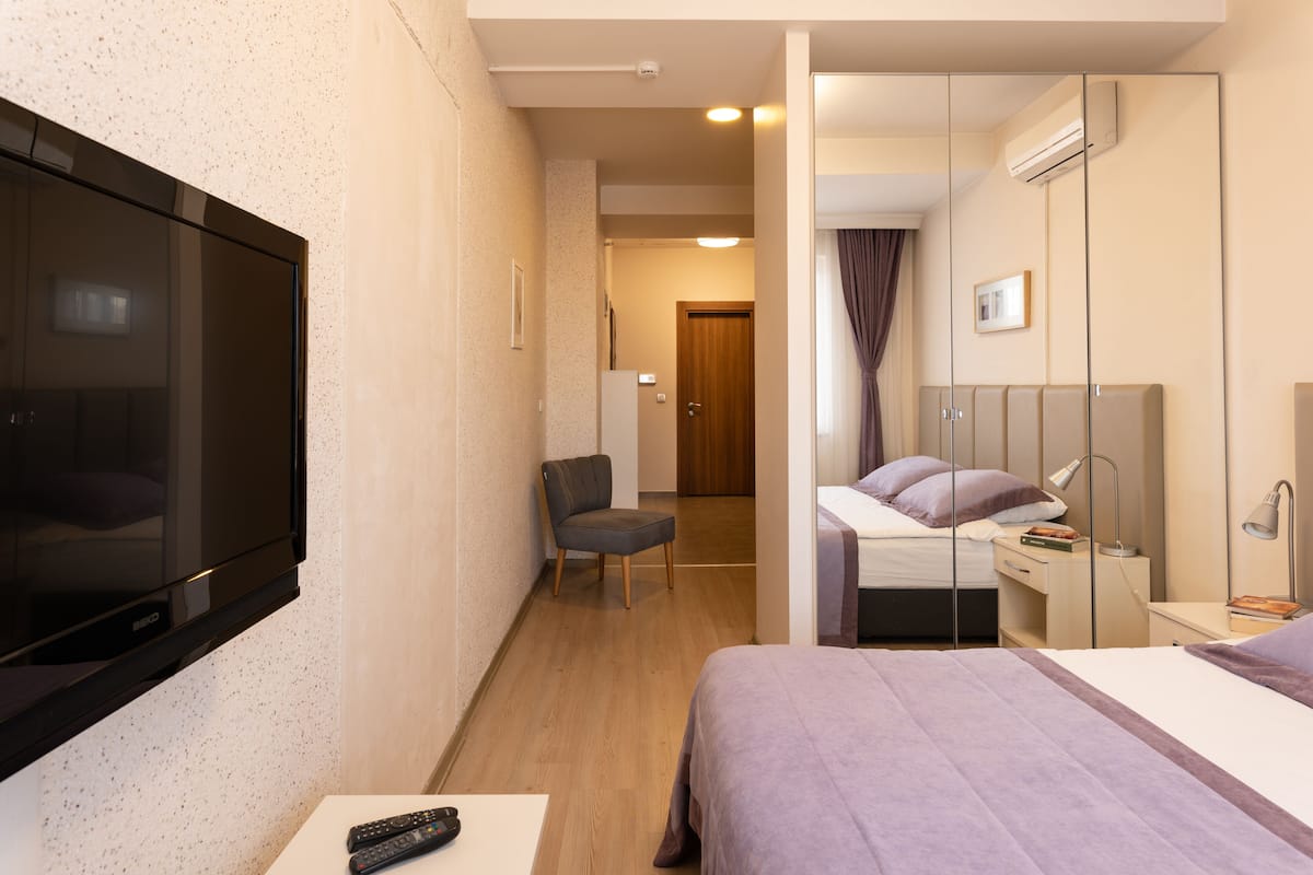 A hotel room with a TV, a bed, a chair, a desk, and a wardrobe.